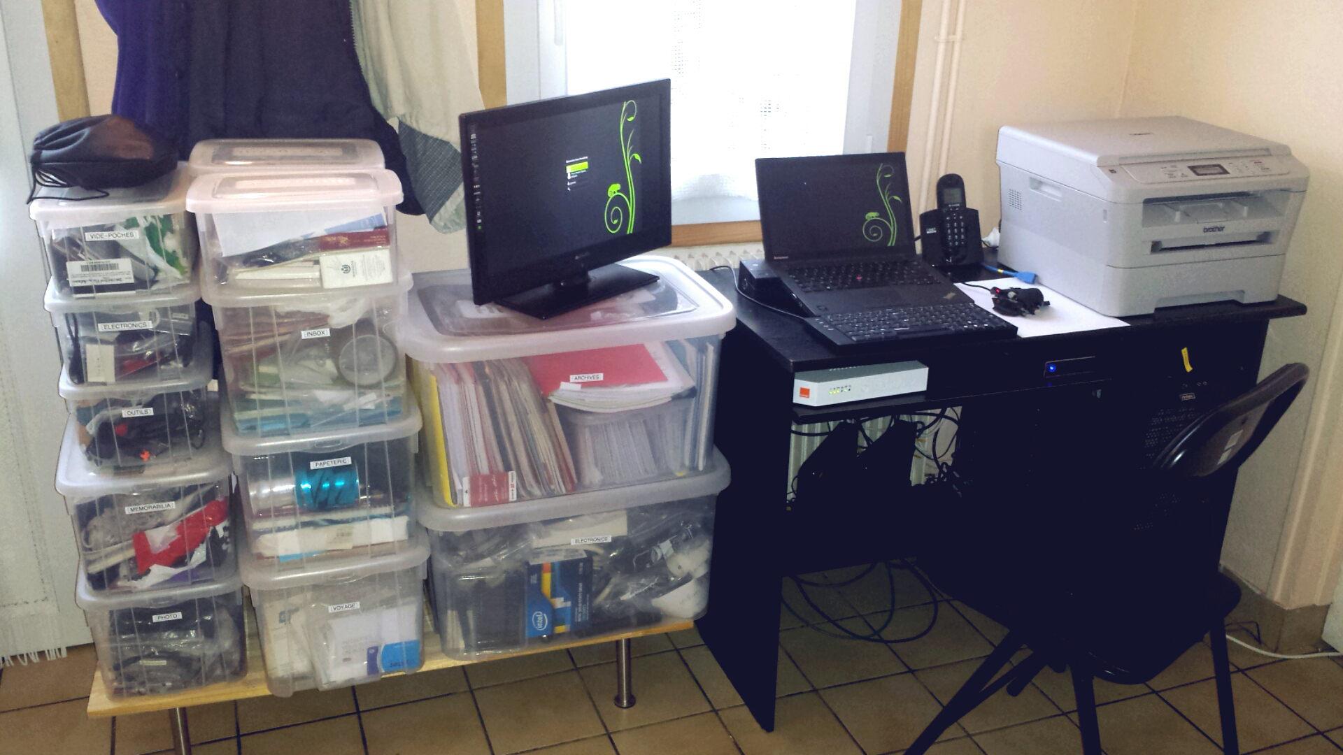 A work station set up on an desk in front of a window, next to a stack of plastic boxes.