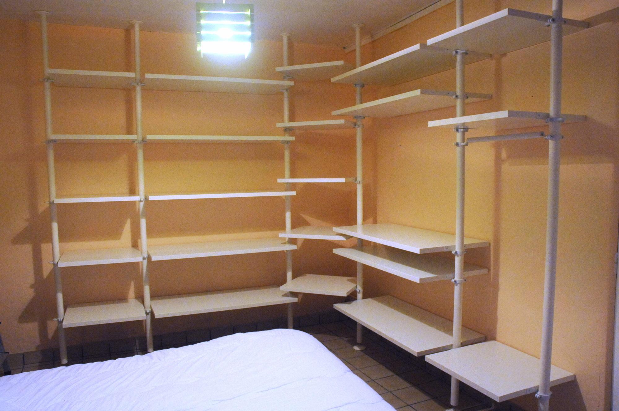 Two walls of a yellow room fitted with five columns of white adjustable shelves held by small pillars.