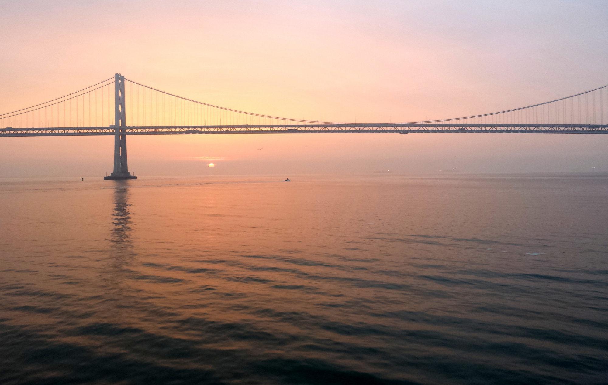 A photo of a sunrise on water with the Bay Bridge in contre-jour.