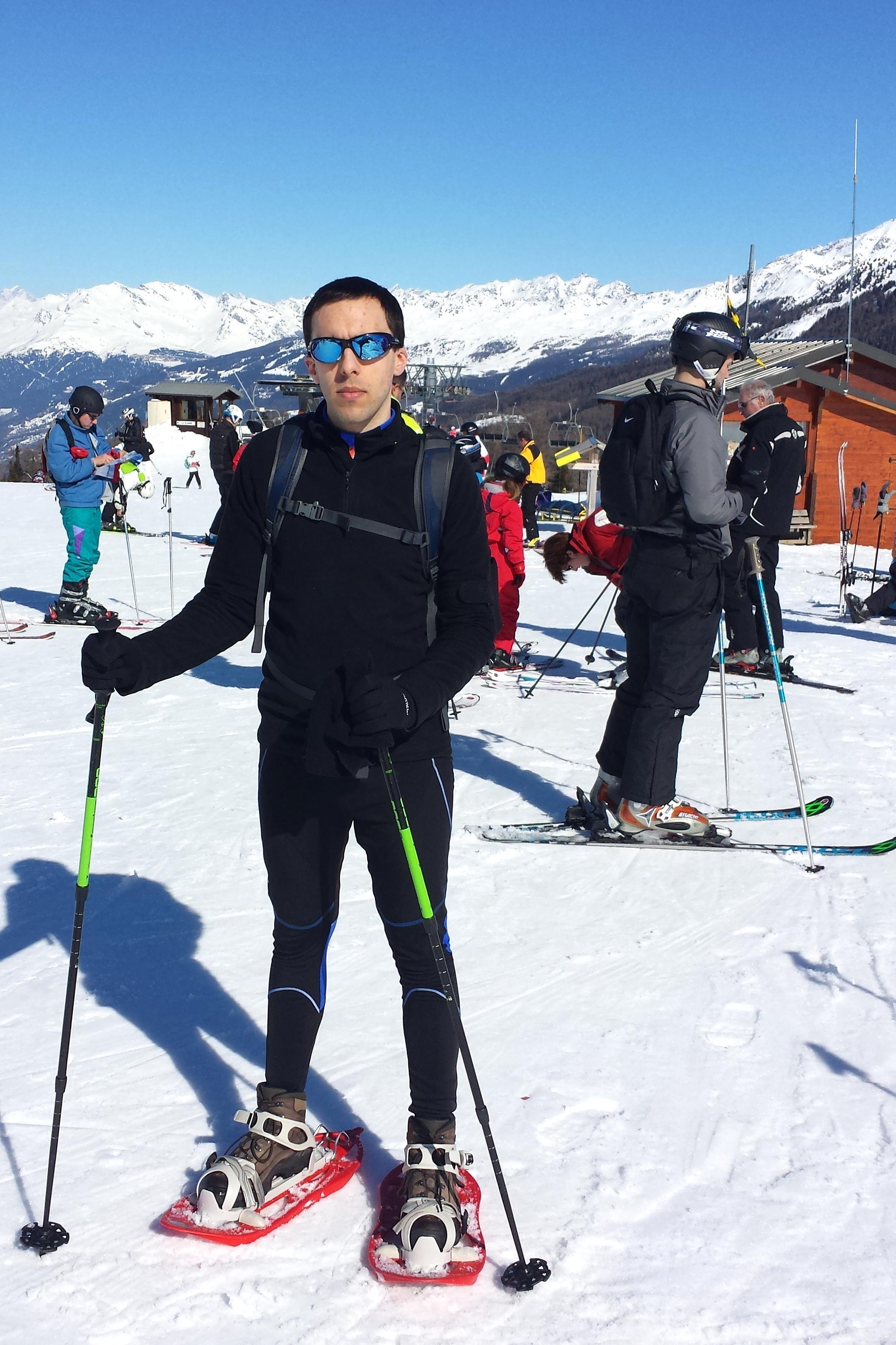 Photo of Guillaume Paumier snowshoeing on top of a mountain, with other skiers and blue skies in the background