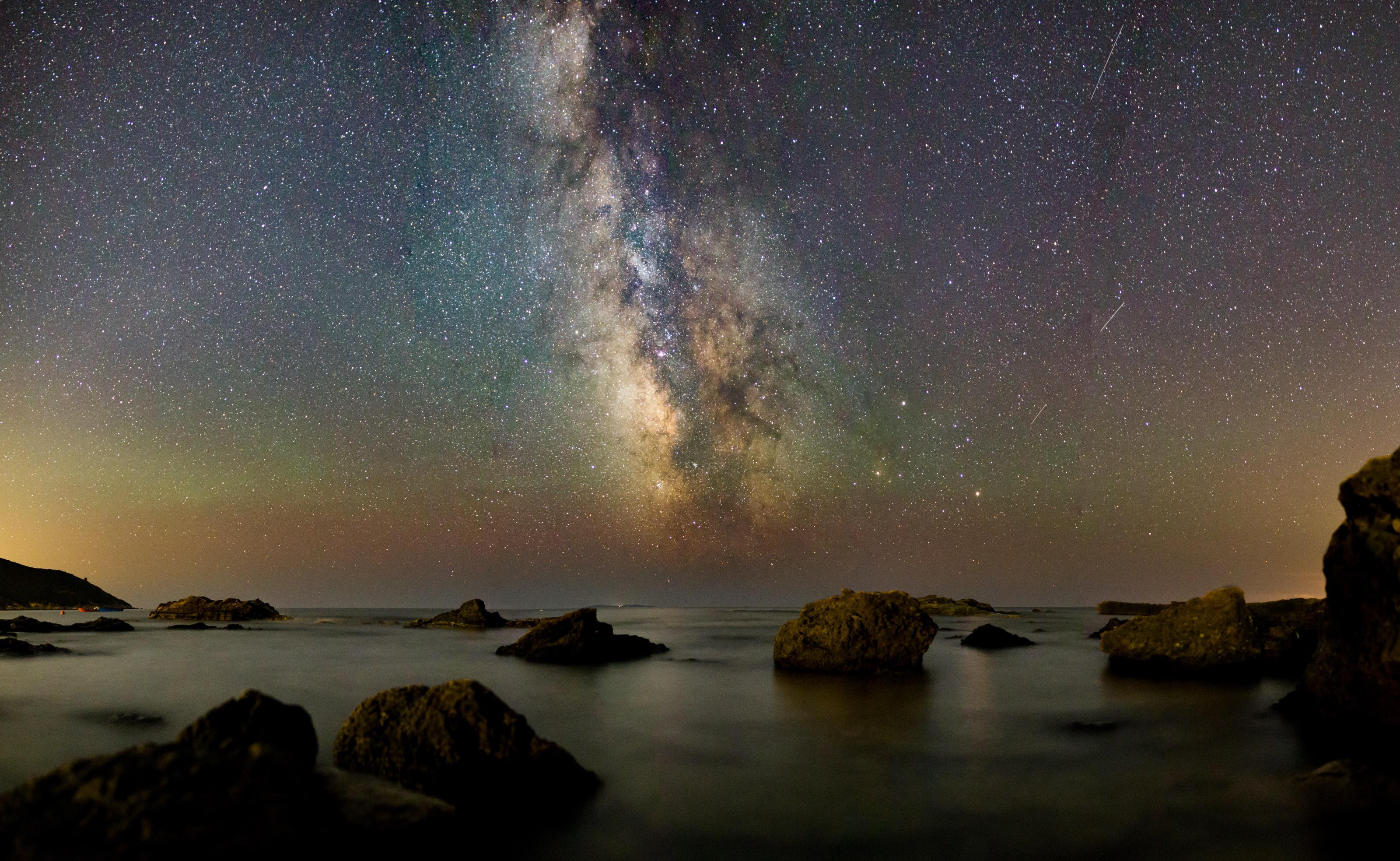 Photograph of rocks in water under a big sky full of stars and showing the Milky Way.