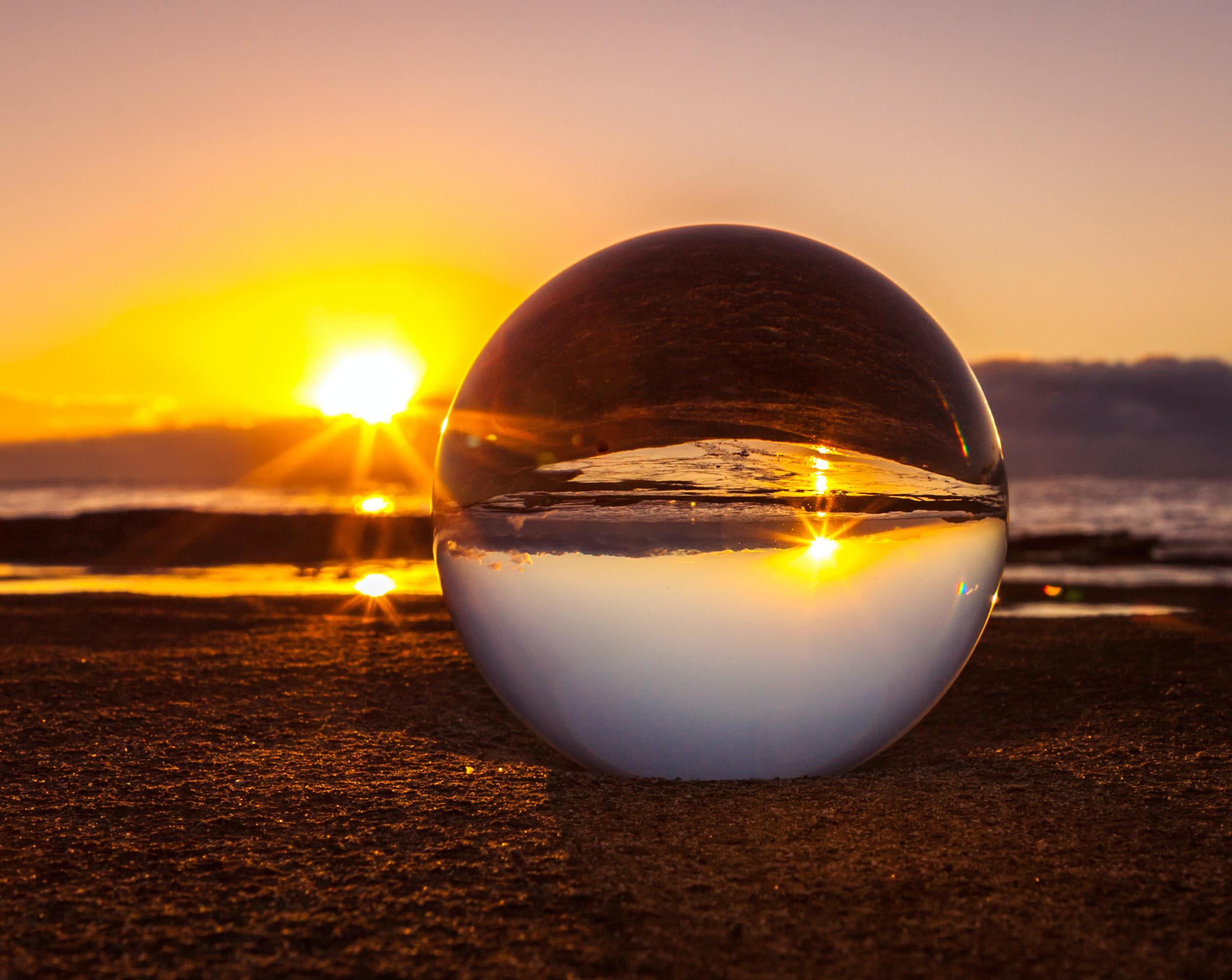 Photograph of a sunset and a glass ball on sand, showing the inverted sunset